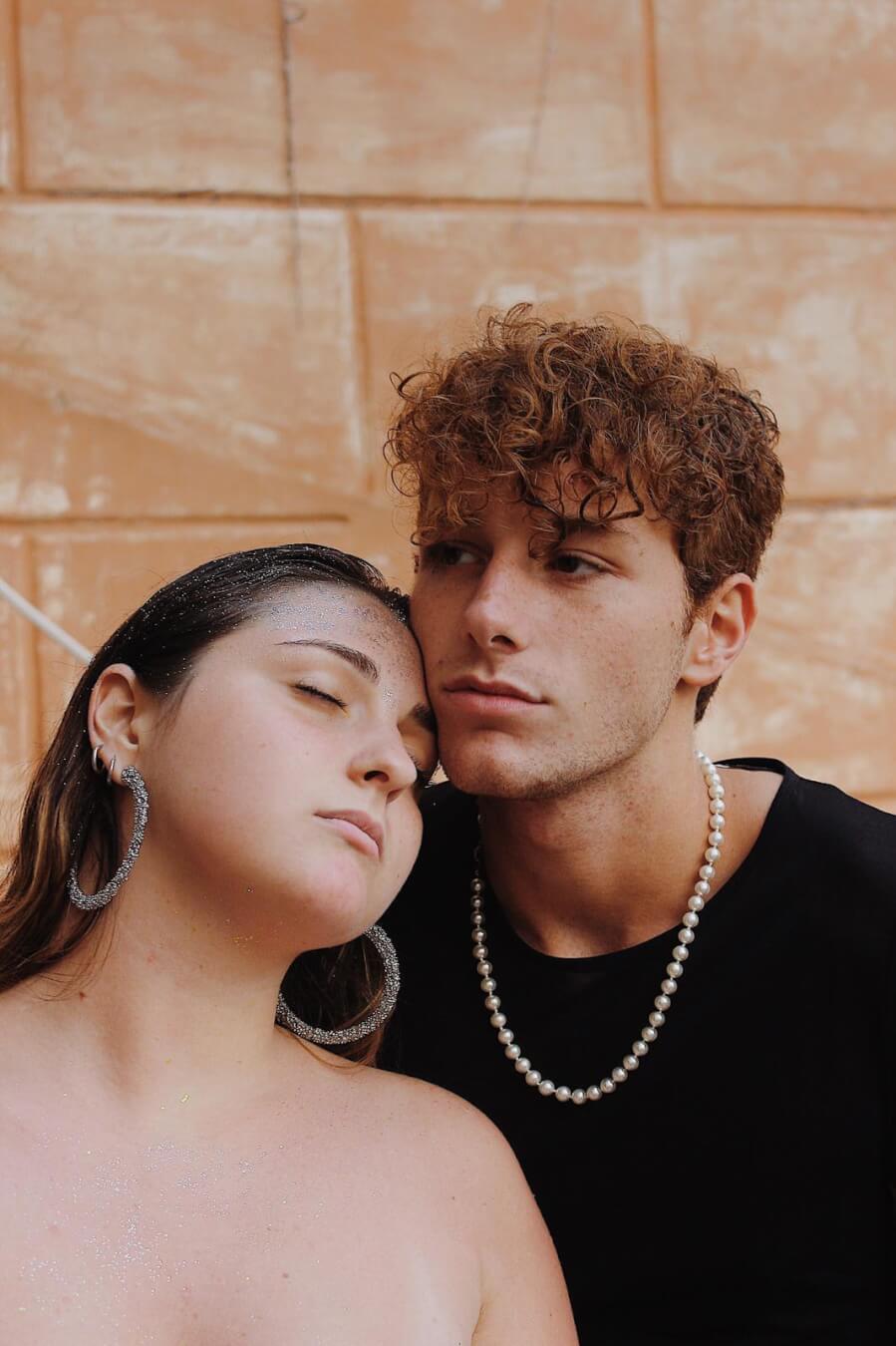 An intimate portrait of a couple with pearl jewelry. The woman has glitter on her face for a dreamy, soft aesthetic.