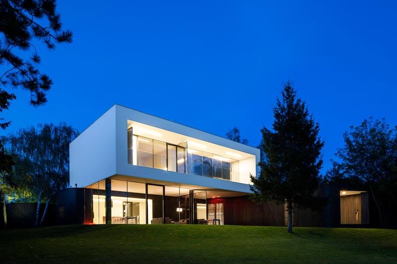 A modern house with sleek design sits on a green lawn under the twilight sky, showcasing contemporary architecture.