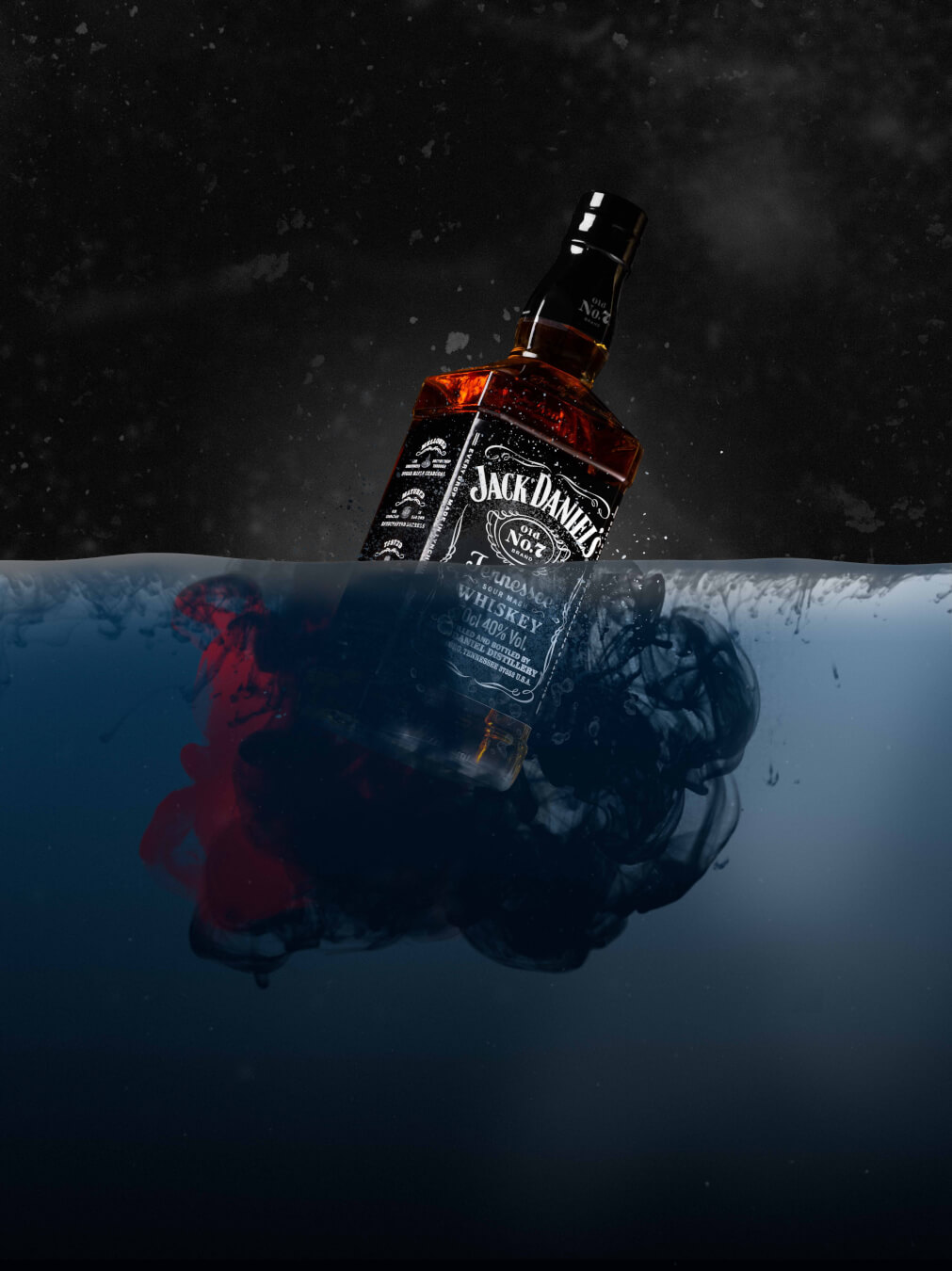 A Jack Daniel's bottle partially submerged in water with dark and red inks swirling around it.