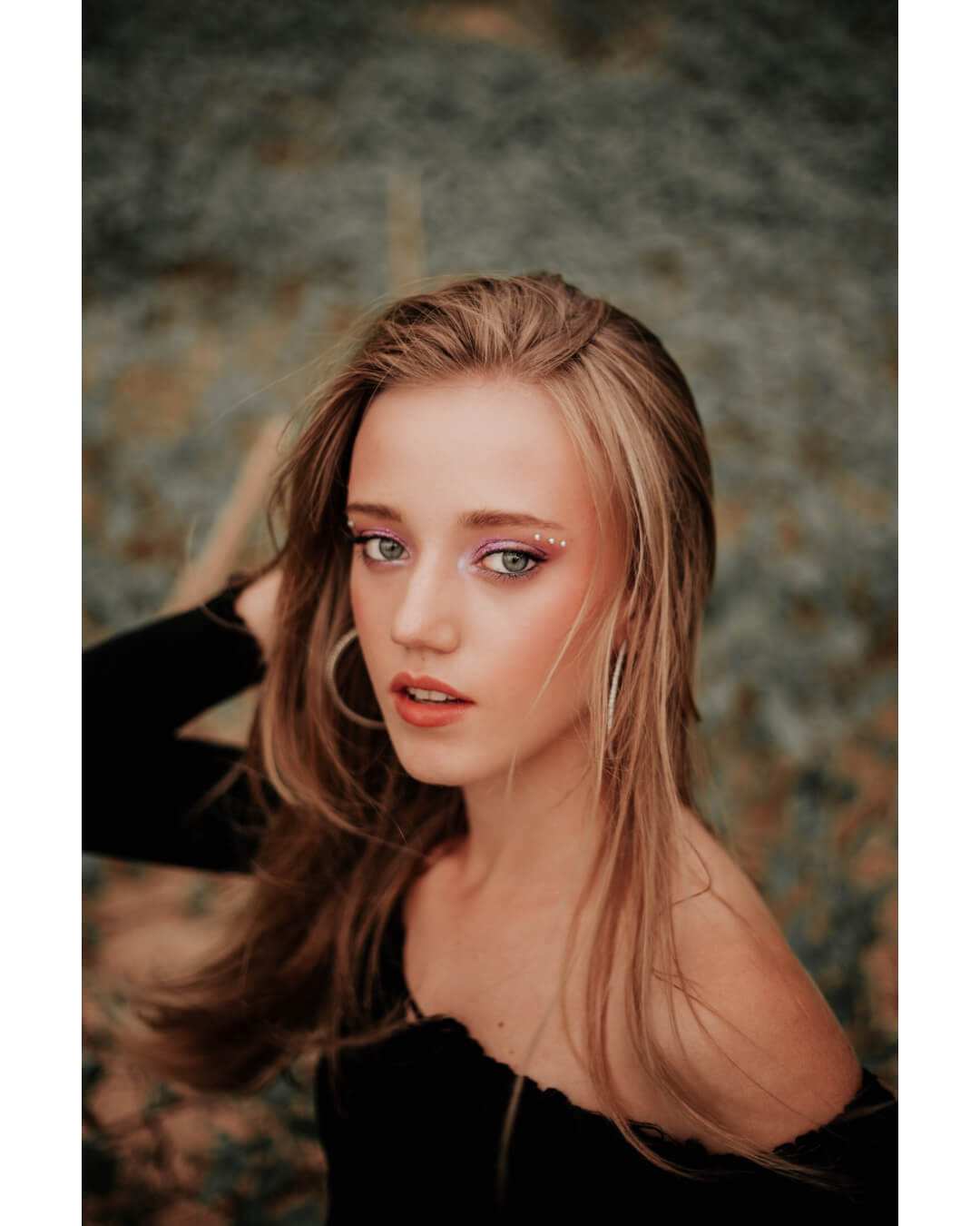 A young woman with blonde hair poses with artistic make-up in a dreamy, close-up editorial style.