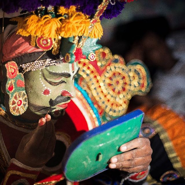 A Kathakali dancer in full makeup applies finishing touches, showcasing vibrant Indian culture and traditional performance art.