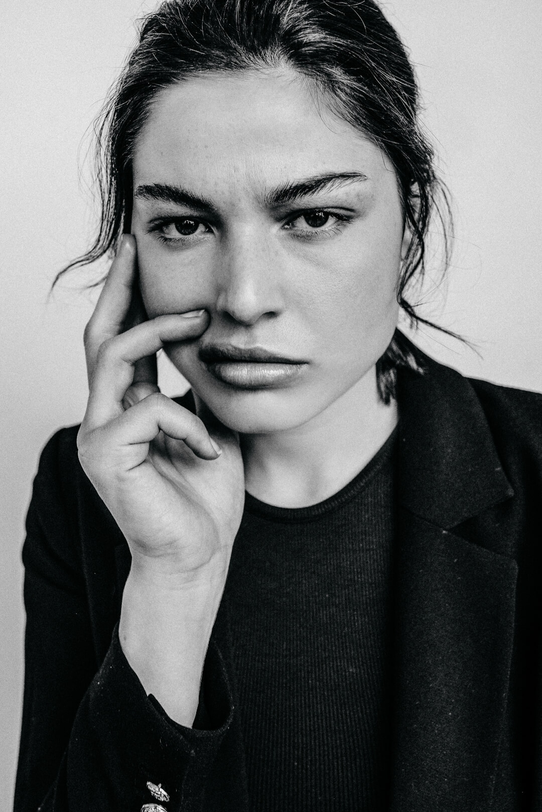 A serious-looking woman in a black jacket poses in a black and white studio portrait.