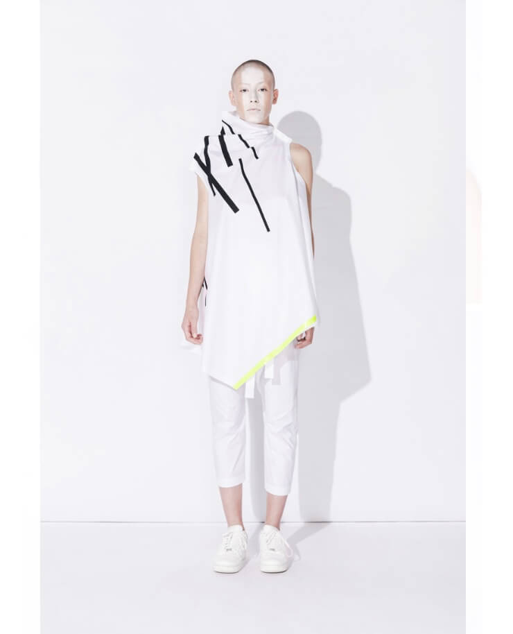A model poses in white avant-garde fashion against a white backdrop for a minimalist editorial fashion shoot.