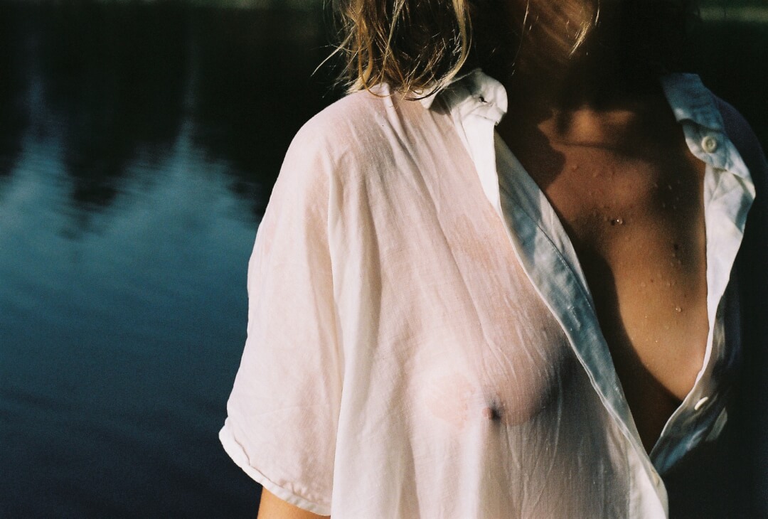 A woman in a white shirt standing by the water, creating a dreamy and sensual atmosphere.