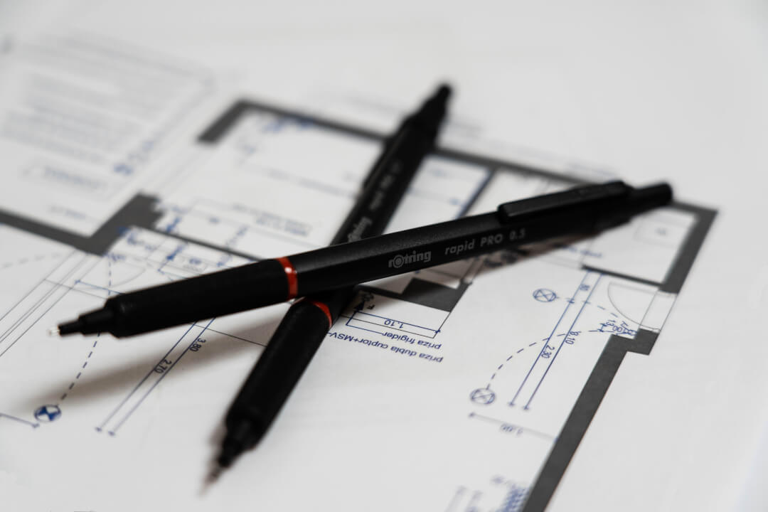 Two Rotring mechanical pencils lay atop an architectural blueprint, tools for design and precision in planning.