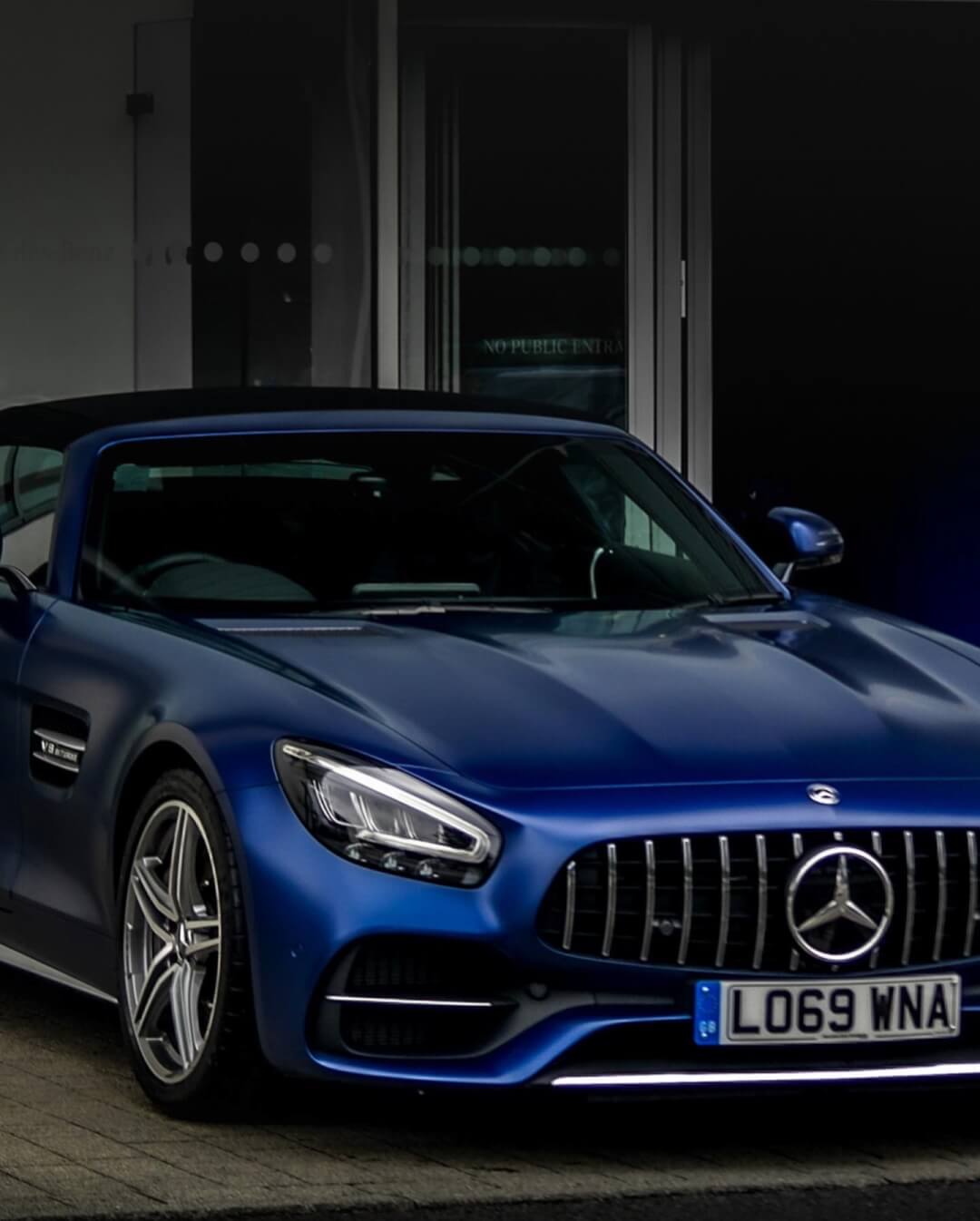 A blue Mercedes-Benz convertible is parked in front of a building. A sleek and luxurious design.