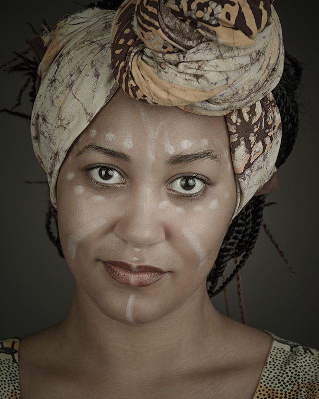 Portrait of a woman with face paint and head wrap, showcasing cultural identity and strength.
