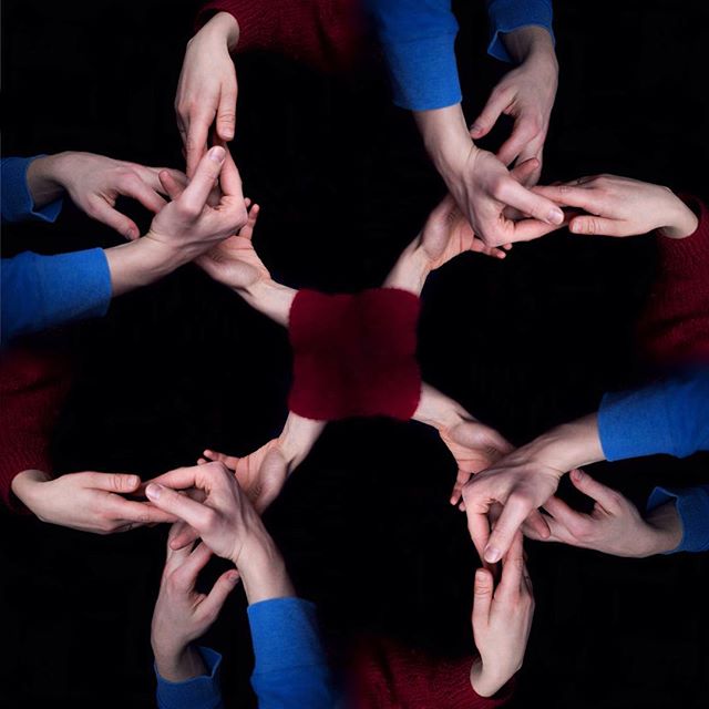 Six people's hands and arms form a collaborative circle, symbolizing unity and connection against a stark black background.