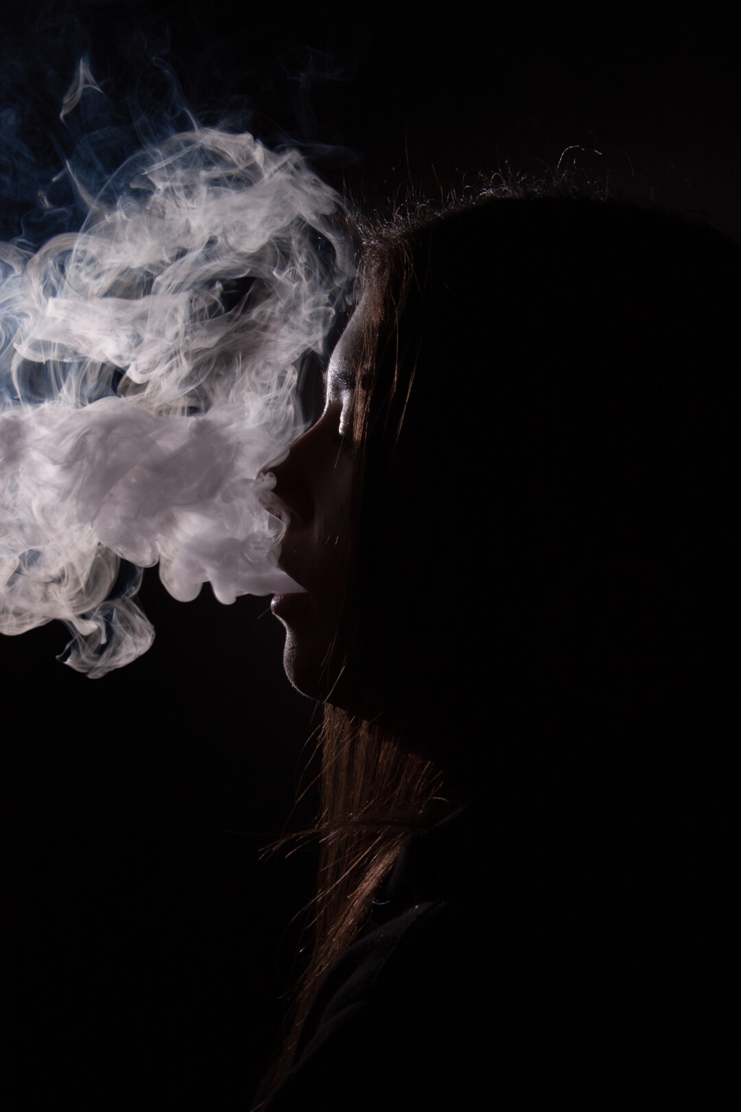 A silhouetted woman exhales a cloud of smoke in a dimly lit, artistic composition.