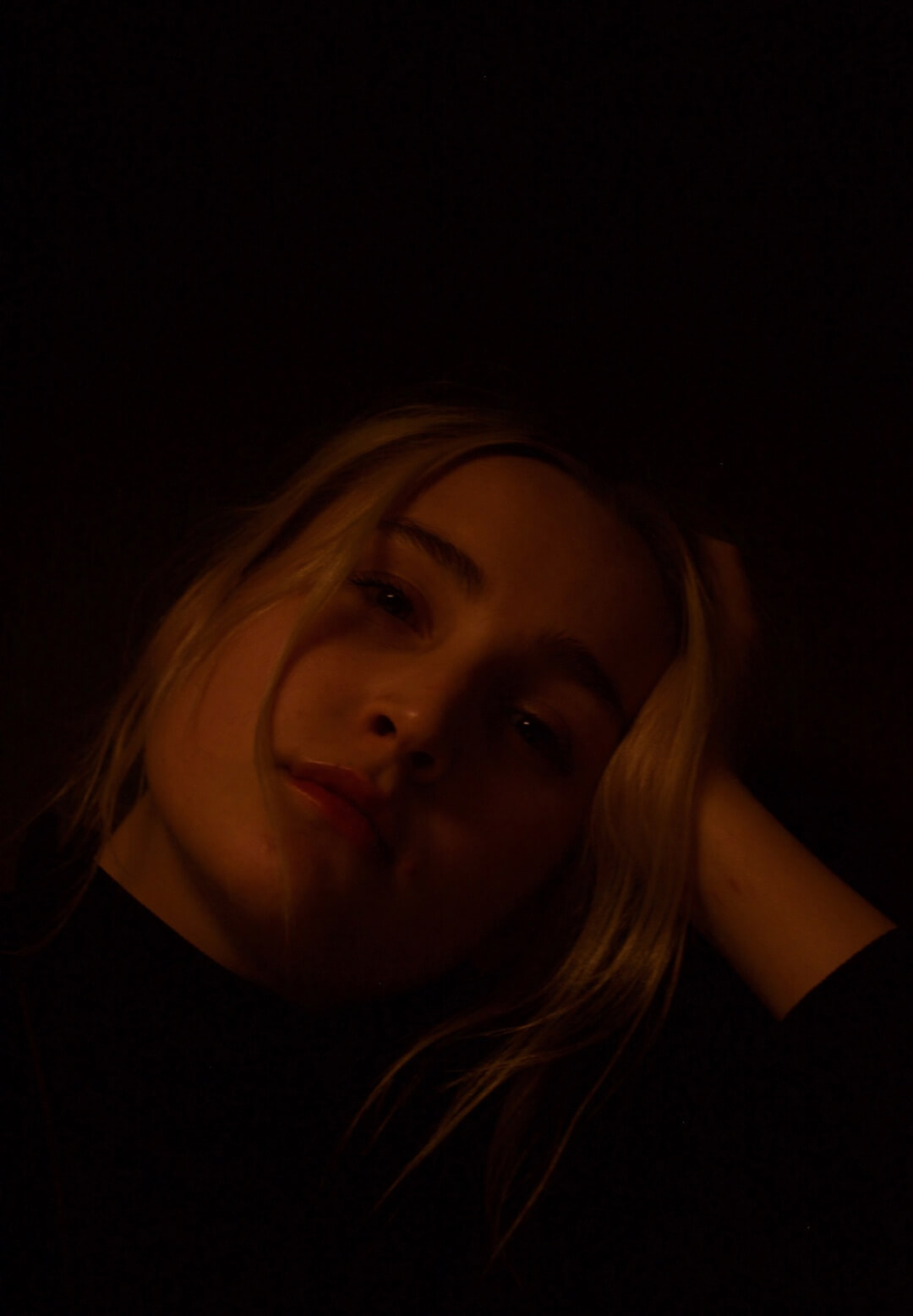 Intimate portrait of a woman with blonde hair in soft, warm lighting against a dark background.