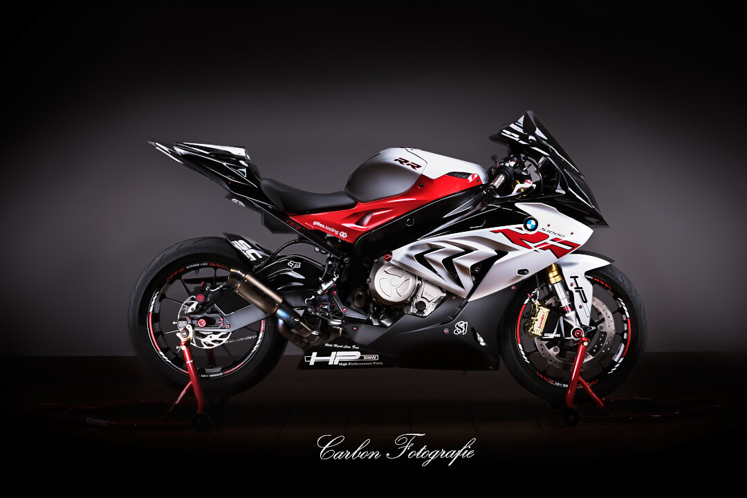 A BMW S1000RR sports bike with a red, white, and black color scheme is shown against a dark backdrop.