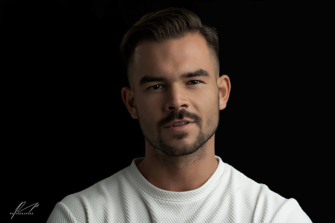 A confident man with short hair poses in a studio setting against a dark background.
