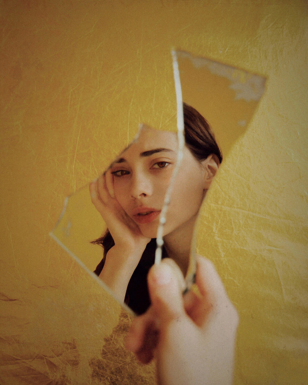 A woman gazes through broken mirror shards in a surreal self-portrait, exploring themes of reflection and identity.