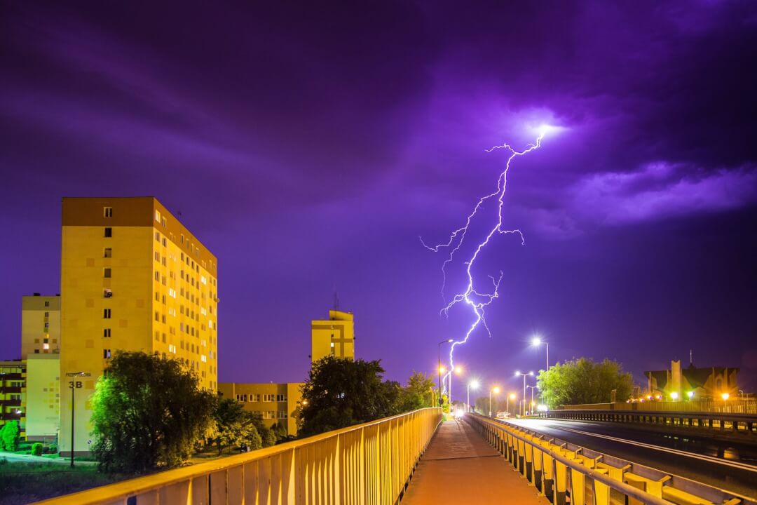 Dramatic lightning strikes illuminate the night sky over a vibrant cityscape, showcasing urban resilience during a storm.