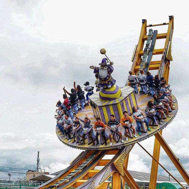 People enjoy a spinning wizard-themed amusement park ride on a cloudy day.
