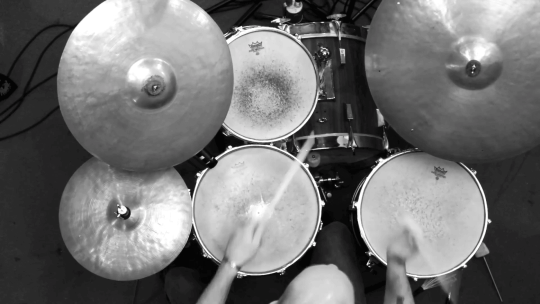 Overhead view of a drummer playing a drum set with cymbals in a black and white shot.