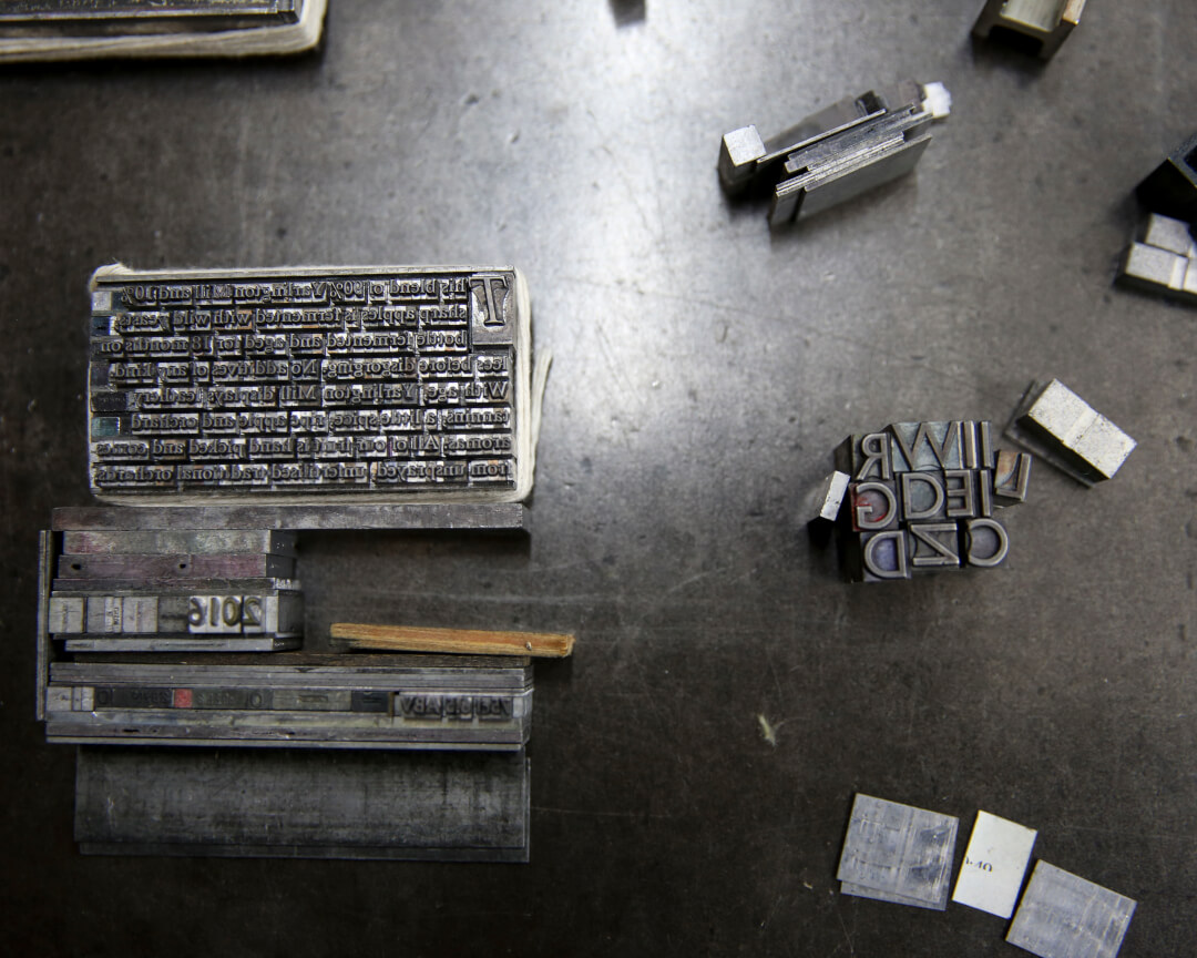Metal letterpress blocks and type used in traditional printing methods, with a vintage industrial aesthetic.