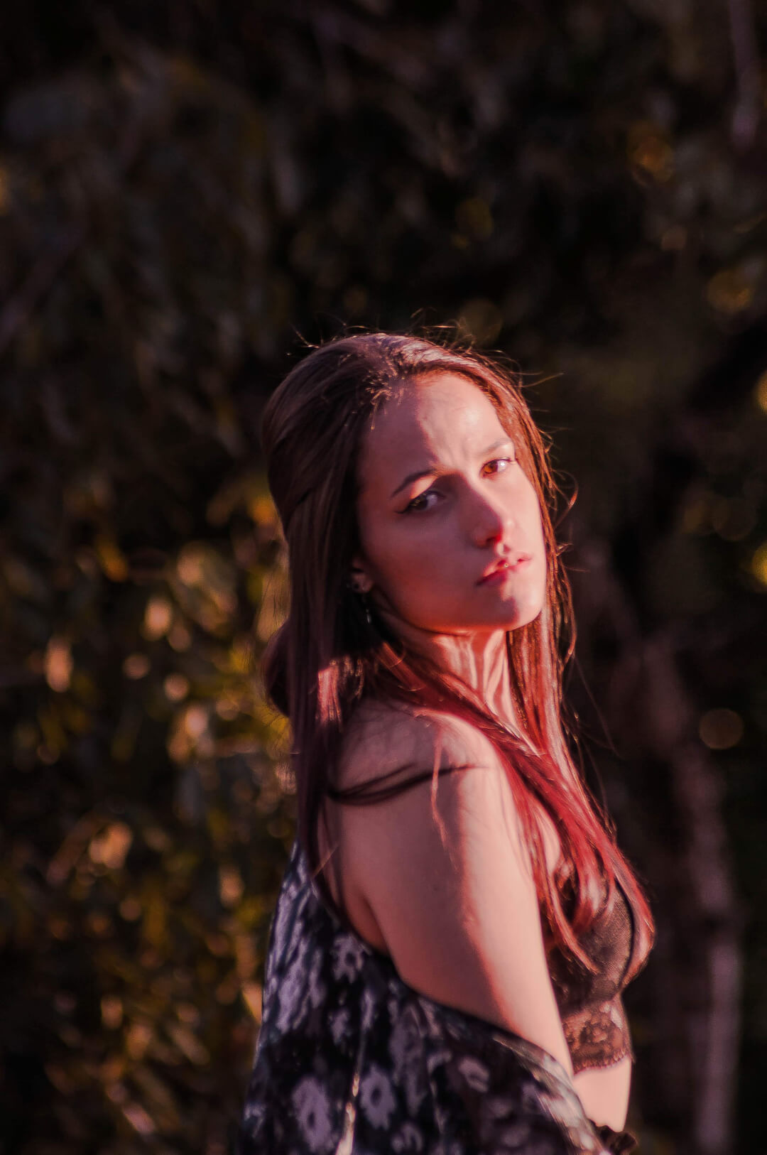 A brunette woman in soft lighting poses outdoors for a sensual fashion or beauty editorial.