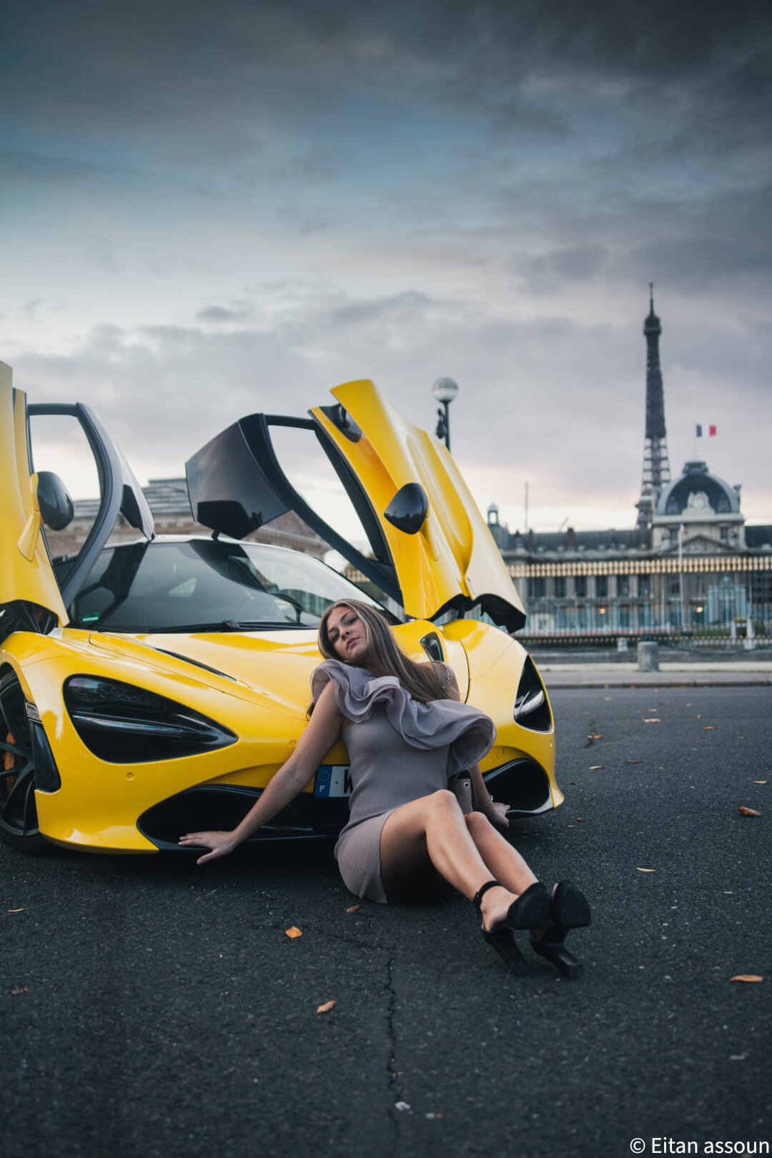 A stylish woman poses with a yellow McLaren in Paris, with the Eiffel Tower in the background.