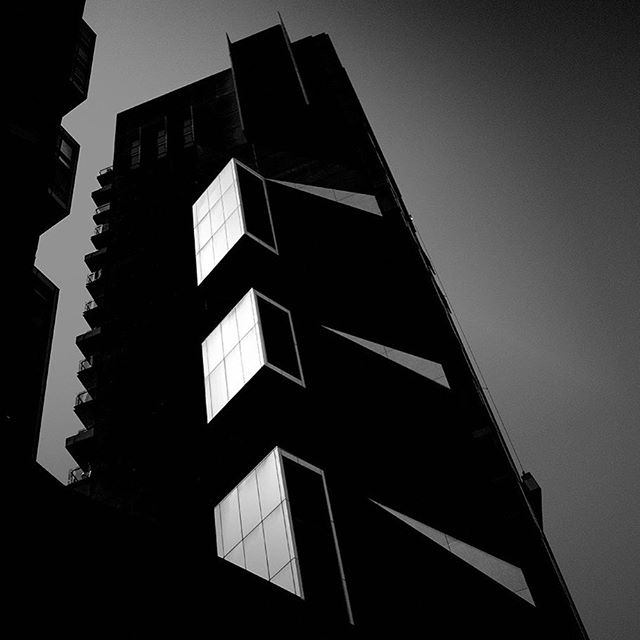 A low-angle, black and white image of a modern building with bold windows and geometric lines against the sky.