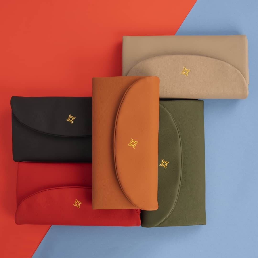 A collection of colorful leather wallets and clutches arranged in a modern, minimalist flat lay studio setting.