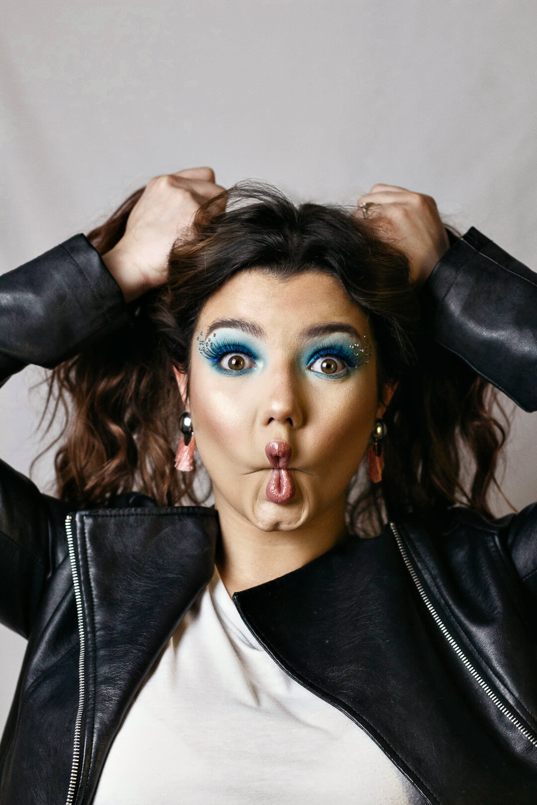 A playful brunette woman with bright blue eyeshadow makes a funny face at the camera.