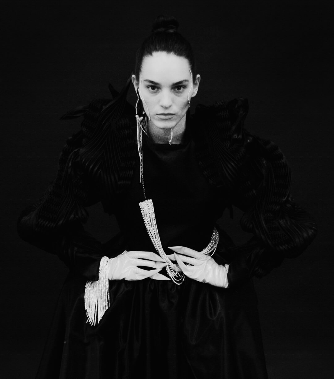 A fashion model in black and white with elegant jewelry poses in a dramatic, high-fashion editorial style.