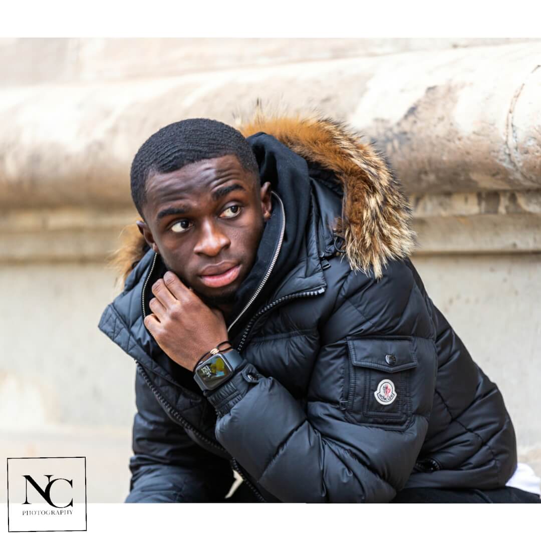 A stylish man in a Moncler winter jacket poses in an urban outdoor setting, showcasing fashion and confidence.