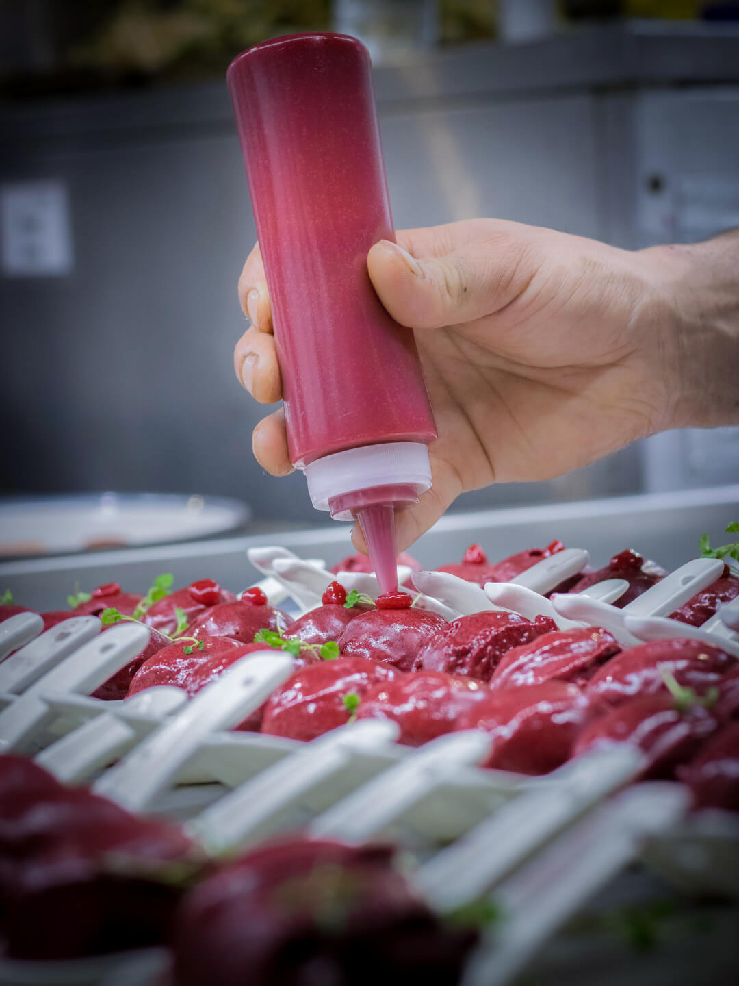 A hand drizzles red sauce on plated desserts, presenting a vibrant close-up shot ideal for social media or food advertising.