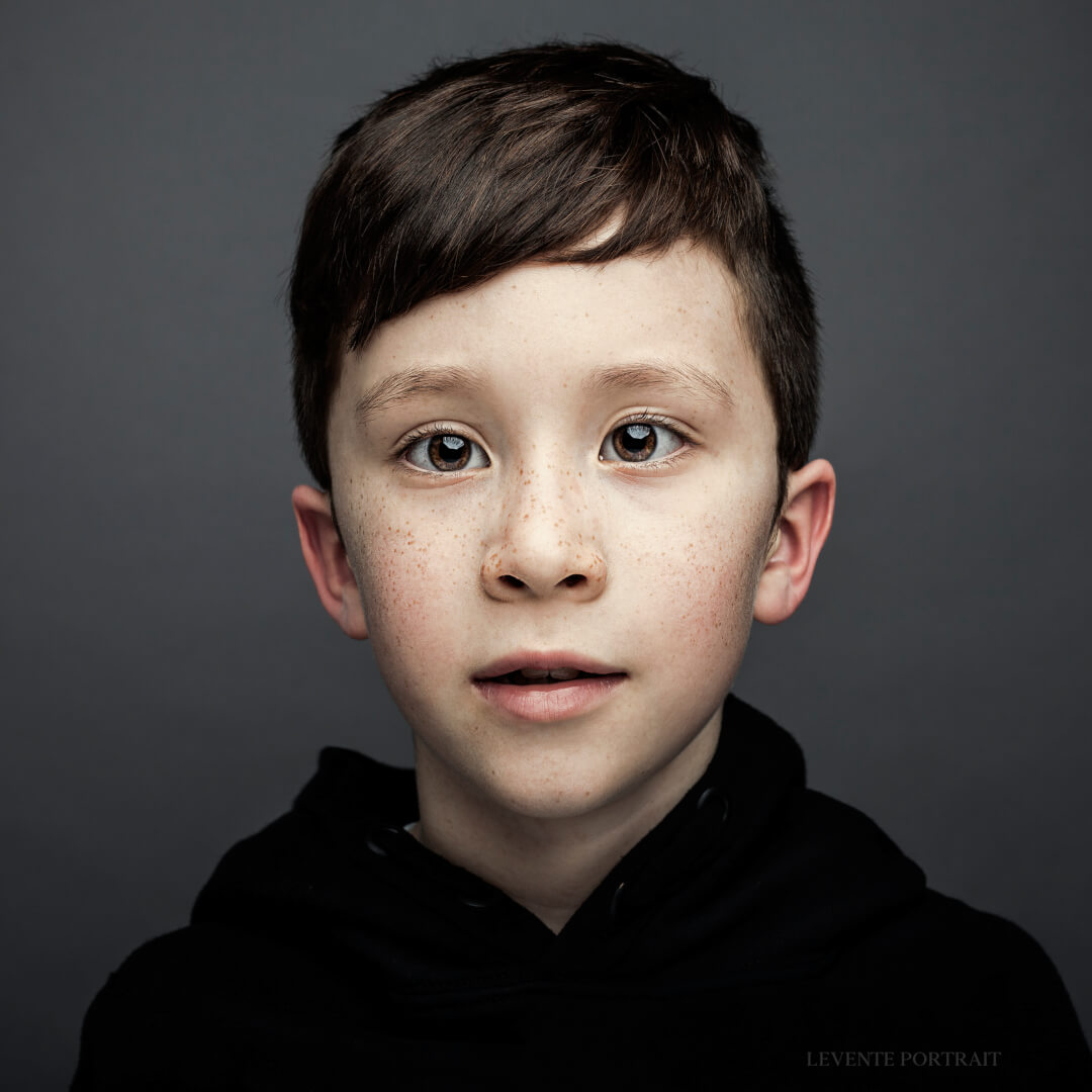 Portrait of a young boy with brown hair and freckles wearing a black hooded sweatshirt.