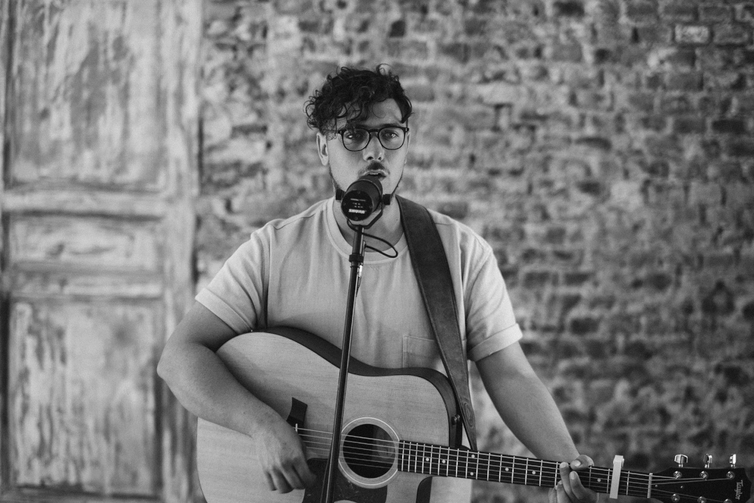 A musician passionately performs with his guitar and microphone in a black and white, vintage style setting.