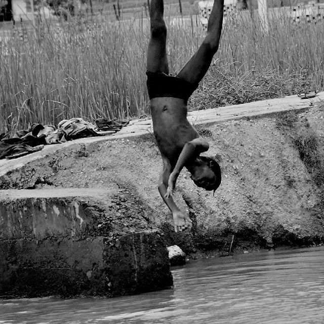 A young boy dives headfirst into a river in black and white.