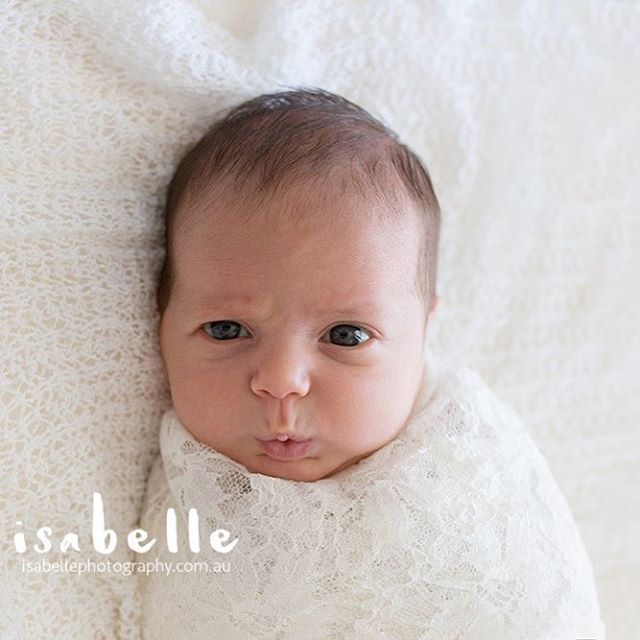 A newborn baby is wrapped in a delicate white blanket, creating a dreamy and tender scene.