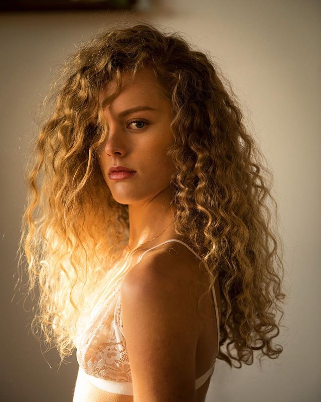Portrait of a beautiful young woman with curly hair wearing lingerie, shot with soft, natural lighting.