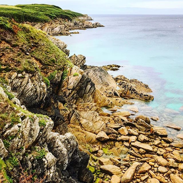 A rocky coastline meets the tranquil sea, featuring rugged cliffs and clear water.
