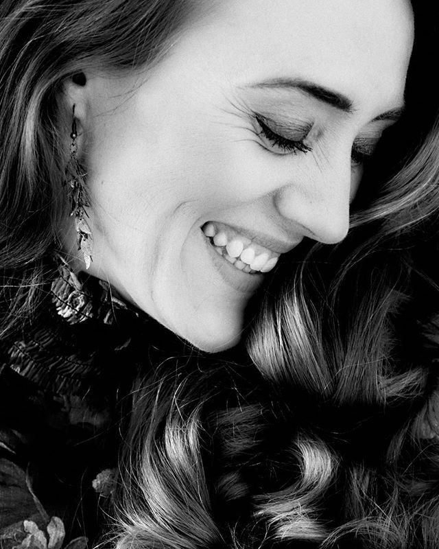 A black and white portrait of a smiling woman with wavy hair looking down. 