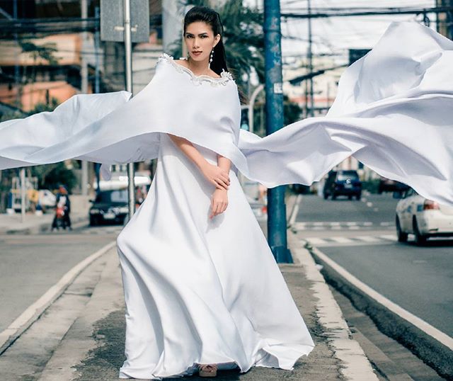 A woman in a white gown and cape stands on a city street, creating an elegant fashion moment.