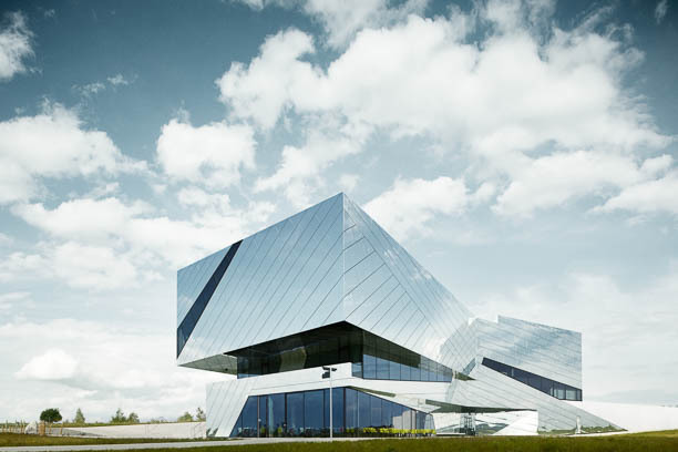 A modern, mirrored building stands under a bright sky with scattered clouds, showcasing innovative architecture.