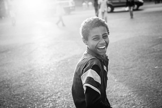 A happy young boy smiles brightly at the camera in a black and white outdoor setting.