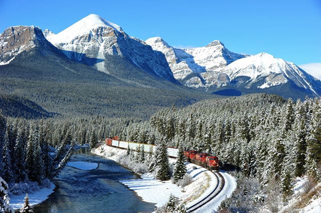 A scenic winter landscape featuring a train winding through snow-covered mountains and a river.