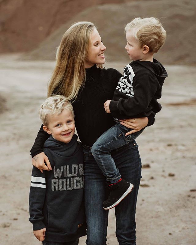 A mother holds her two young sons in a field, sharing a loving moment in a candid lifestyle shot.