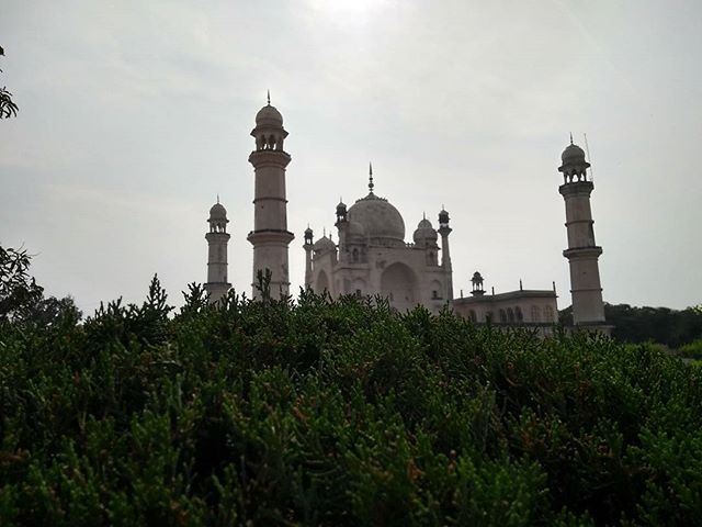 The Bibi Ka Maqbara mausoleum rises behind green bushes under a soft sky in Aurangabad, India, a beautiful historical landmark.