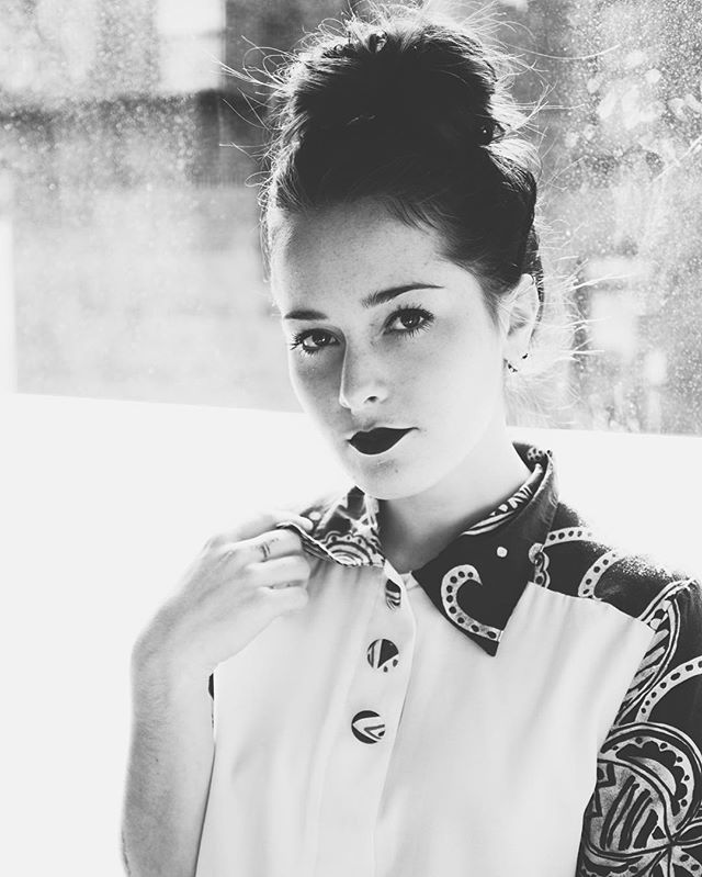 A woman with a bun hairstyle poses in black and white, creating an intense and moody editorial portrait.