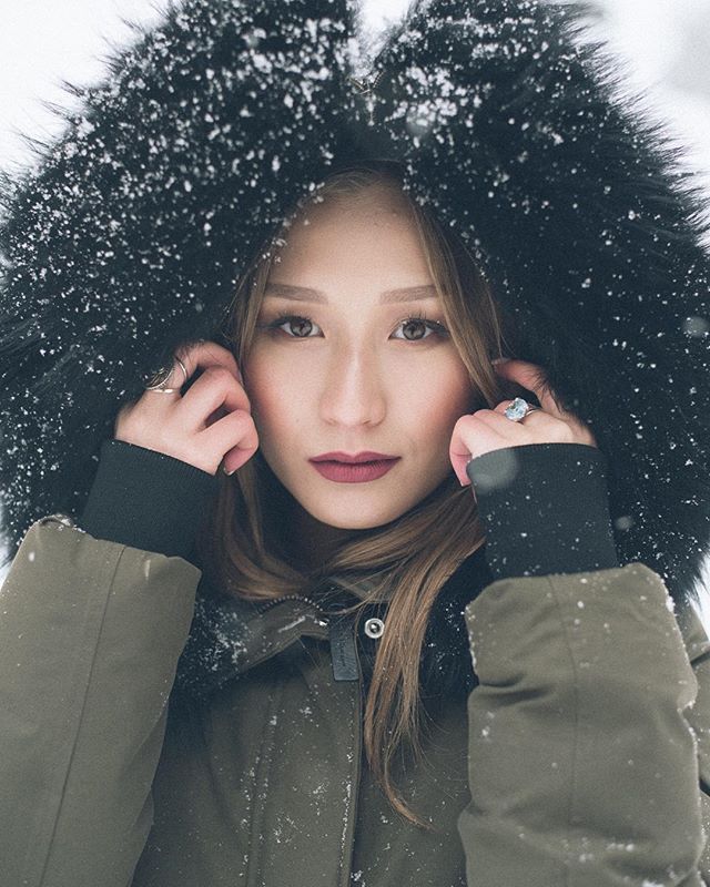 A woman in a fur-trimmed hood stands in a snowy scene, a portrait of winter serenity and style.