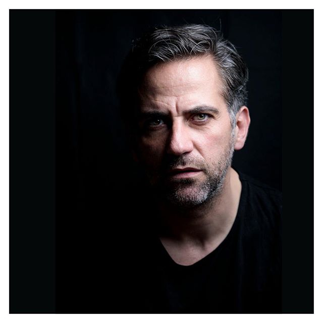 A dramatic headshot of a man with a serious expression against a dark background.