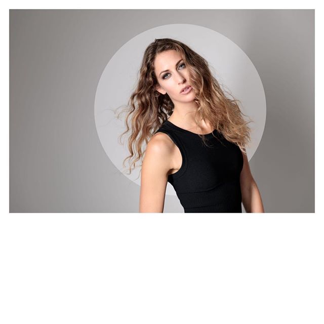 A confident woman with wavy hair poses in a studio setting, showcasing natural beauty and style.