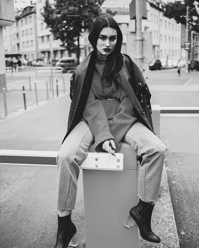 A stylish woman sits on a city street smoking a cigarette in a monochrome fashion shot.