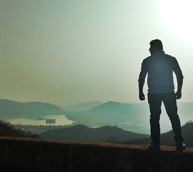 A man stands on a hilltop, gazing at the misty mountain landscape, creating a scenic and thoughtful moment.