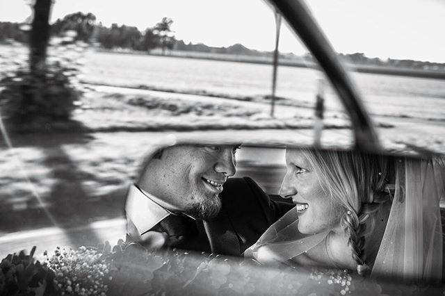 A happy bride and groom are reflected in the mirror of their wedding car.