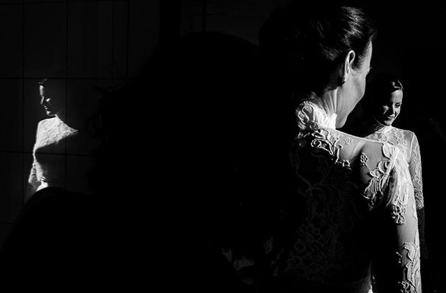 A bride is seen in black and white with soft lighting as she admires herself in a mirror.